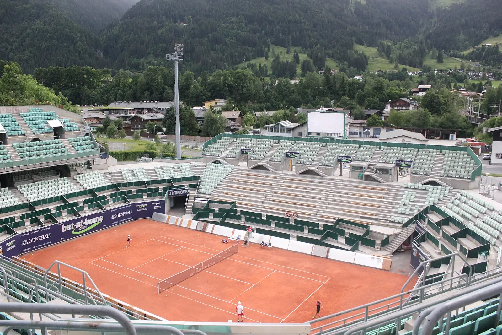 Clay court and stands of the Kitzbuehel tennis stadium with wooded hills behind