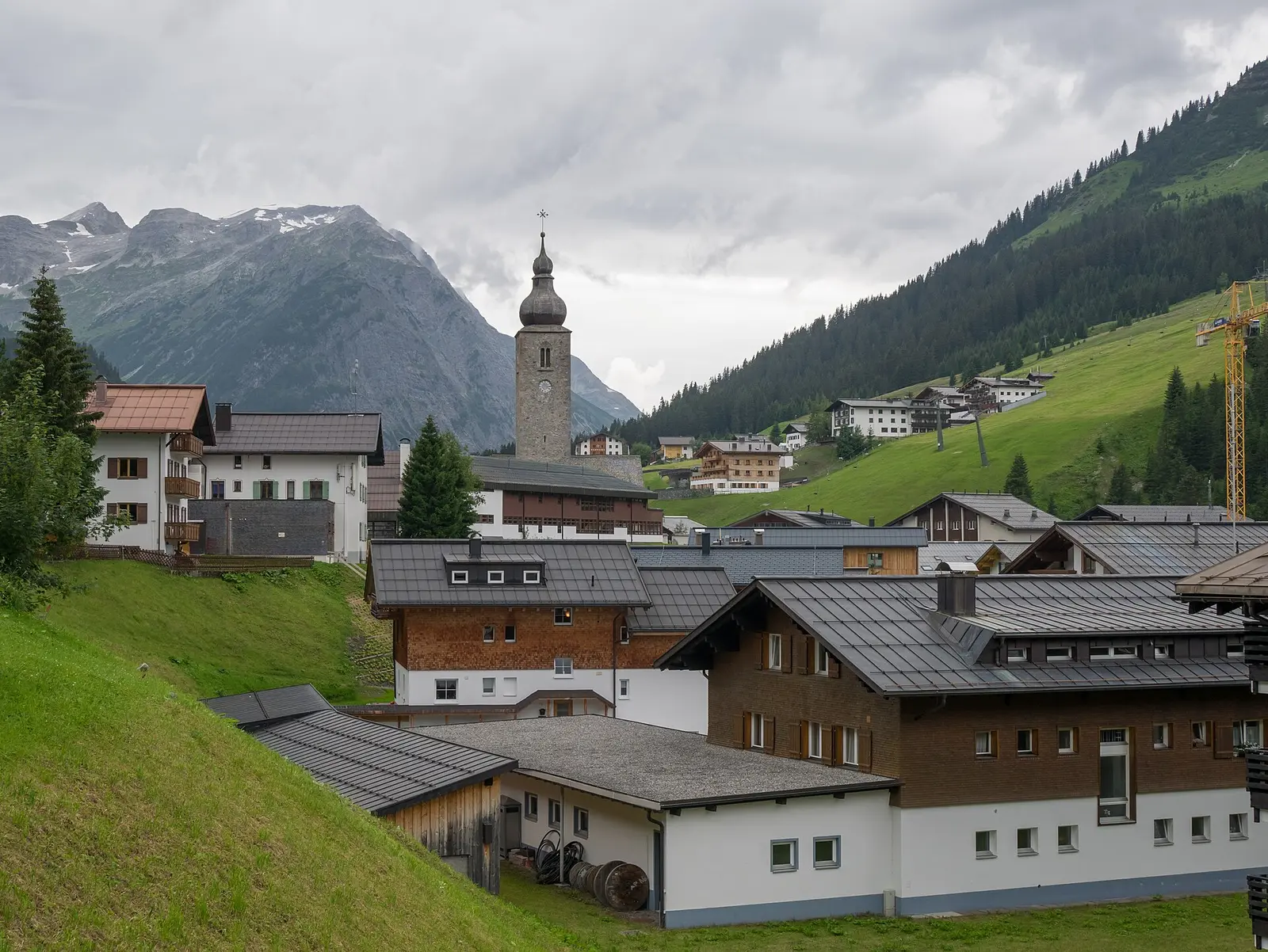Church tower and chalets of the village of Lech am Arlberg with mountains behind